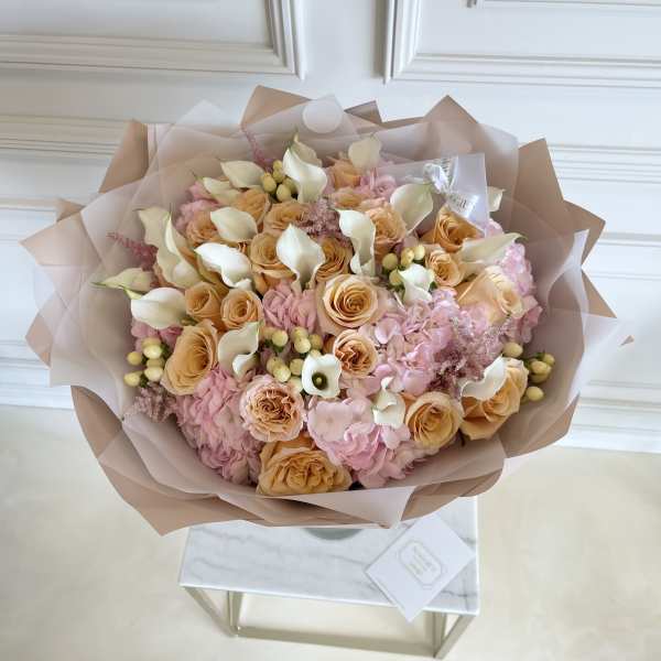 Bouquet of peach roses, pink hydrangeas, and white calla lilies wrapped in blush paper