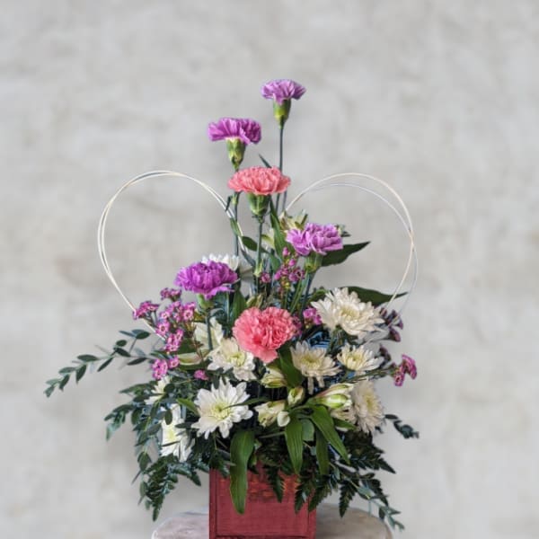 Mixed pink, purple, and white flowers in a red square container with heart loops