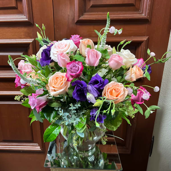 Mixed bouquet of pink, peach, white, and purple roses in a glass vase