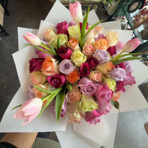 Bouquet of multicolored roses with pink tulips wrapped in white paper