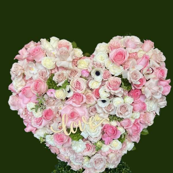 Heart-shaped pink and white rose arrangement with a "love" sign