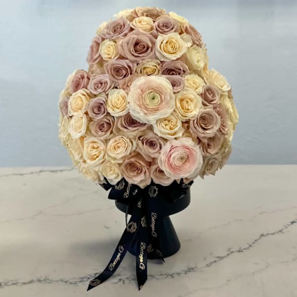 Round bouquet of blush and cream roses in a black ribbon-wrapped base
