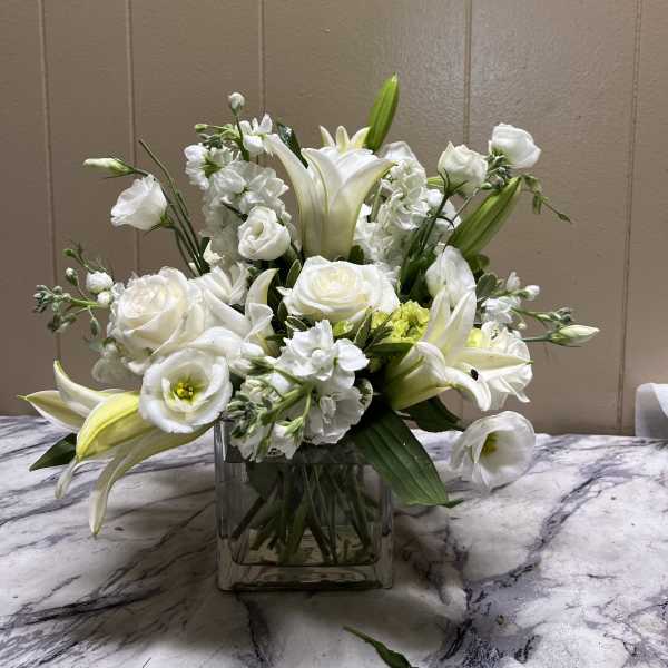White lilies and roses arranged in a square glass vase