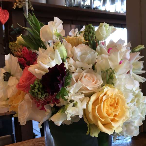 Mixed bouquet of white, yellow, pink, and burgundy flowers in a glass vase