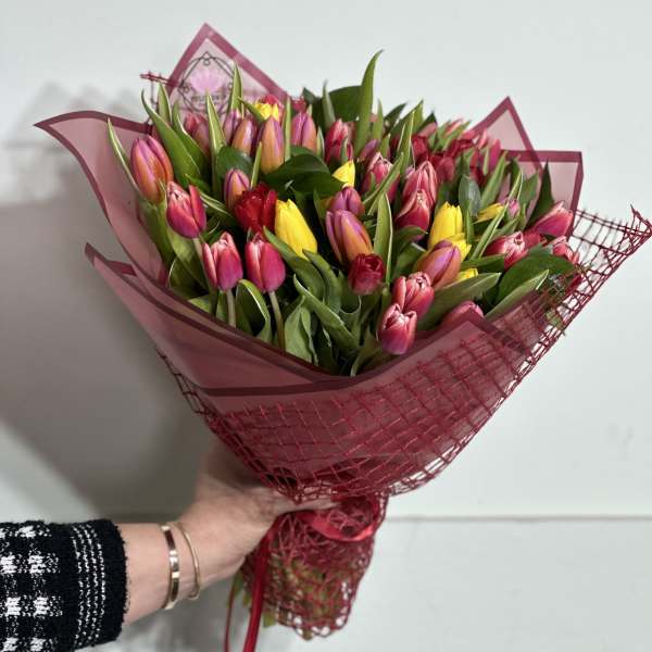 Handheld bouquet of pink, yellow, and orange tulips wrapped in magenta paper