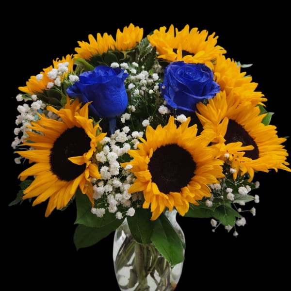 Sunflowers and blue roses arranged in a clear glass vase