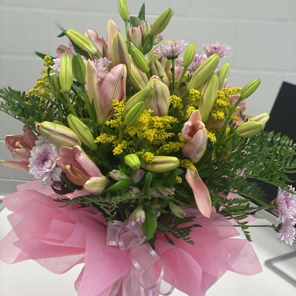 Pink lilies and daisies in a glass vase with pink wrapping