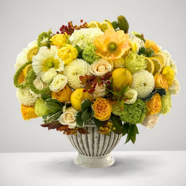 Yellow and white floral arrangement in a striped urn vase with lemon slices