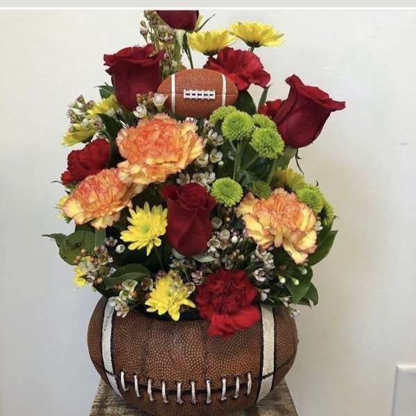 Football-shaped floral arrangement with red roses, carnations, and yellow daisies