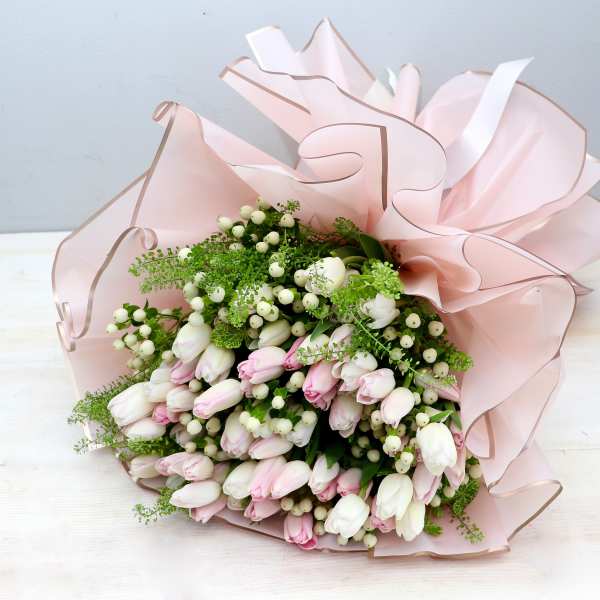 Hand-tied bouquet of white and pale pink tulips with white berries wrapped in ruffled blush paper