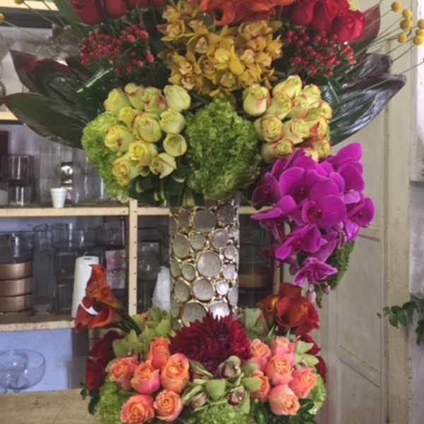 Tall floral arrangement with red, orange, yellow, green, and purple blooms in a decorative vase.