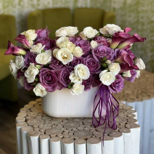 Purple and white rose arrangement in a white vase with calla lilies