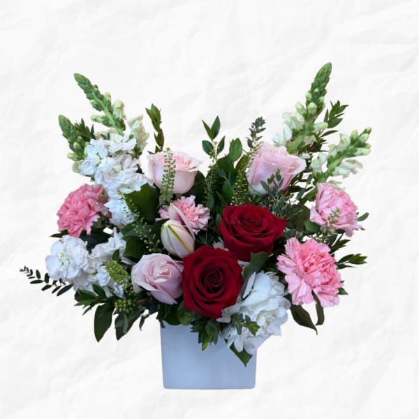 Mixed bouquet of red, pink, and white flowers in a square vase