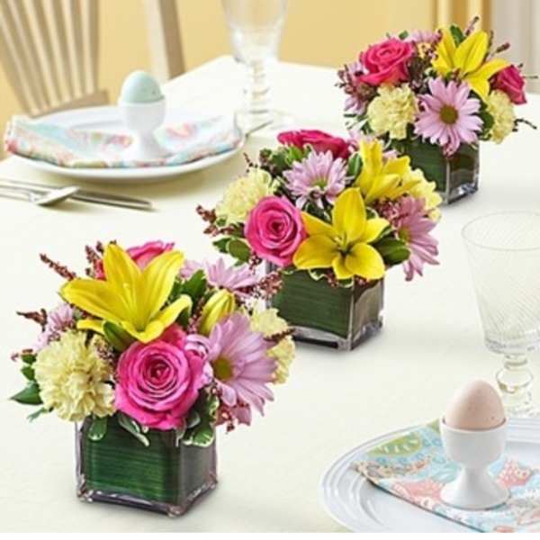 Three small floral centerpieces in square glass vases on a table