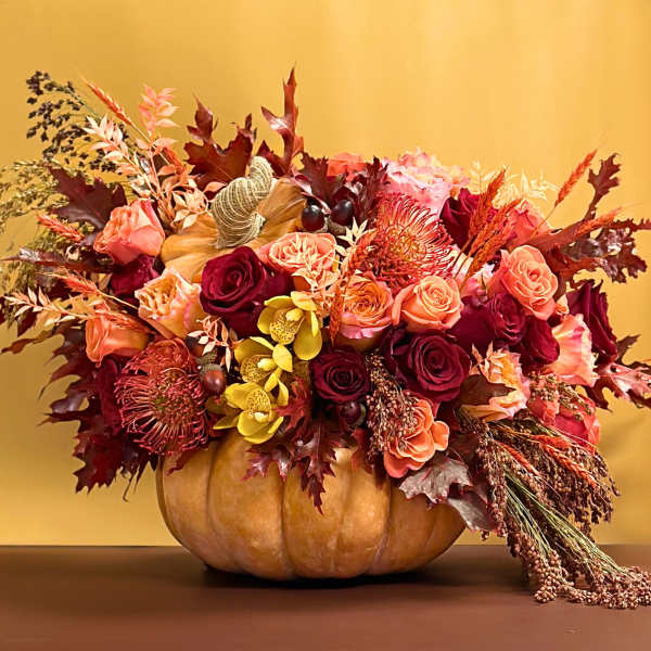Autumn floral arrangement in a pumpkin container with roses and orchids