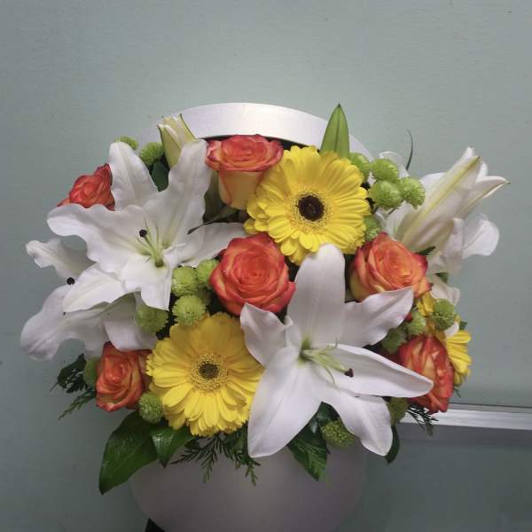 Bouquet of white lilies, yellow gerbera daisies, and orange roses in a white vase