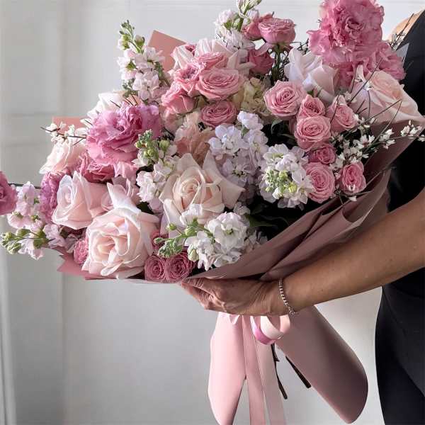 Large pink bouquet of roses and ruffled blooms wrapped in blush paper