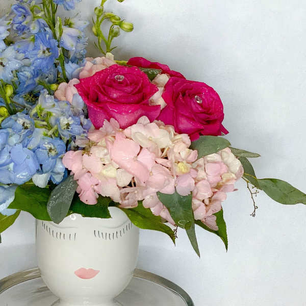 Pink roses and blue hydrangeas in a white face vase