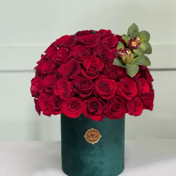 Red rose arrangement in a green cylindrical box with green orchids