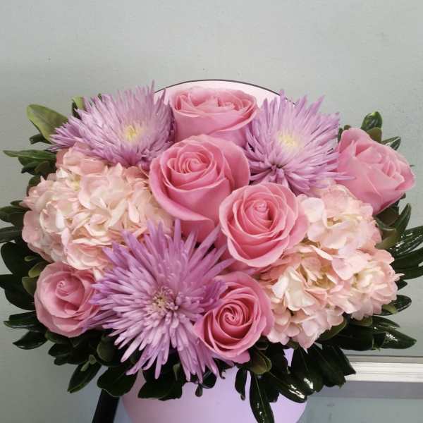 Pink roses and lavender flowers arranged in a round box