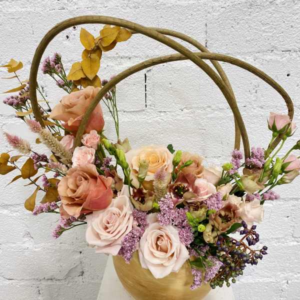 Basket arrangement of peach and pink roses with purple filler flowers