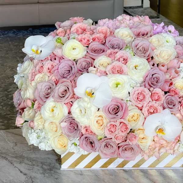 Large pastel bouquet of roses and white orchids in a striped box