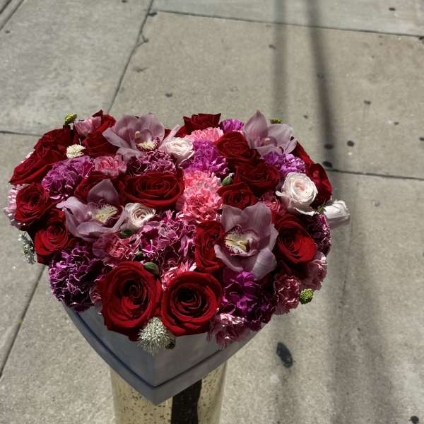 Heart-shaped bouquet of red roses, pink carnations, and orchids