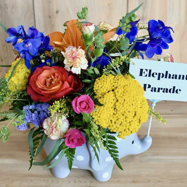 Colorful flower arrangement in a white elephant container with a sign reading Elephant Parade