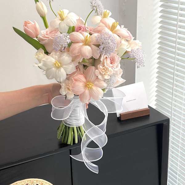 Handheld bouquet of pale pink and white flowers tied with a white ribbon