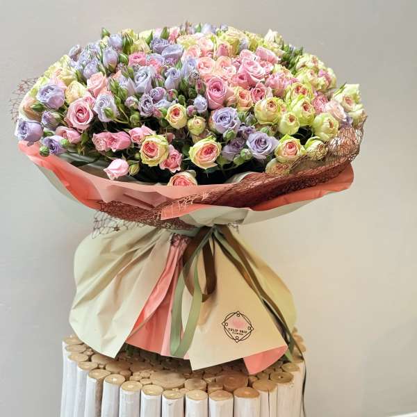 Large bouquet of pastel pink and lavender roses wrapped in cream and pink paper