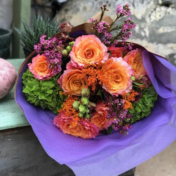 Bouquet of peach roses and purple filler flowers wrapped in lavender paper