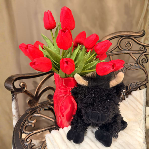 Red tulips in a glossy red vase beside a black plush bull