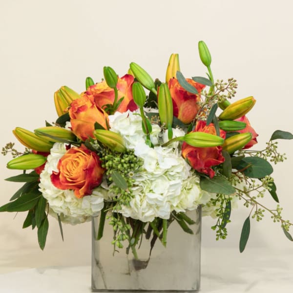 Orange roses and white hydrangeas in a square glass vase