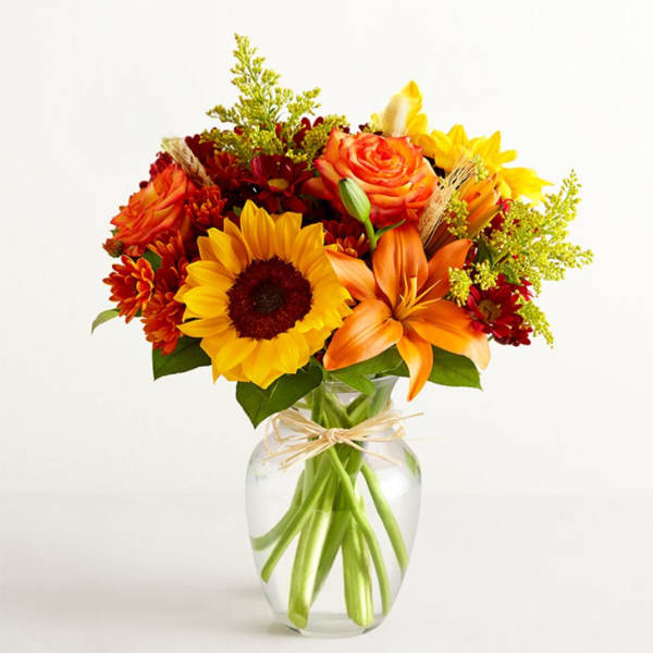 Bouquet of sunflowers, orange roses, and lilies in a clear glass vase