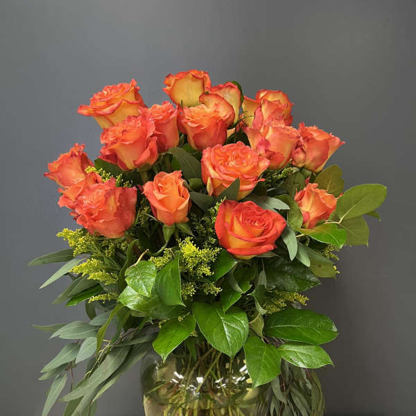 Orange roses arranged in a glass vase with greenery