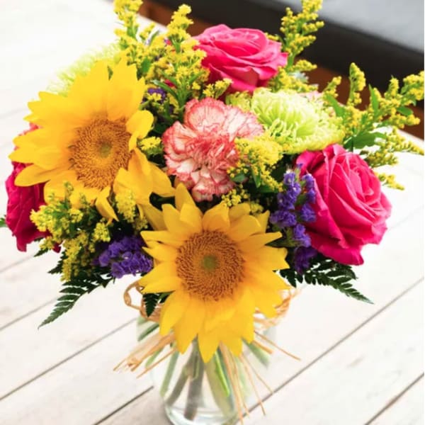 Bouquet of sunflowers, pink roses, and mixed filler flowers in a glass vase
