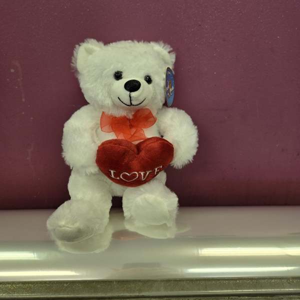 White teddy bear holding a red heart with a ribbon