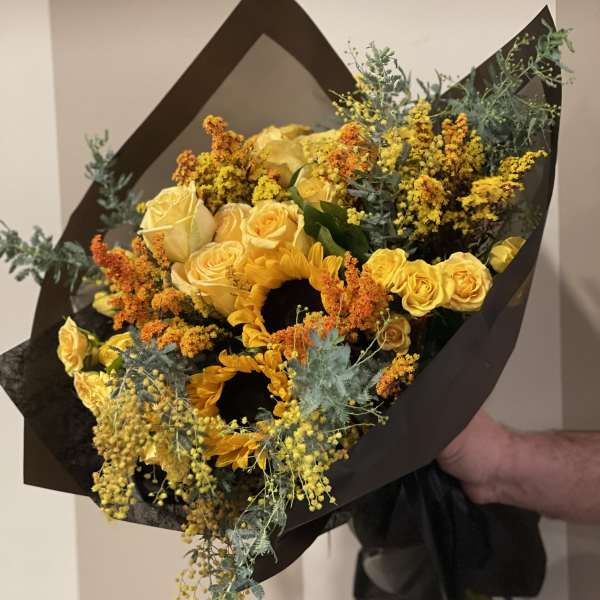 Yellow roses and sunflowers in a dark wrapped bouquet