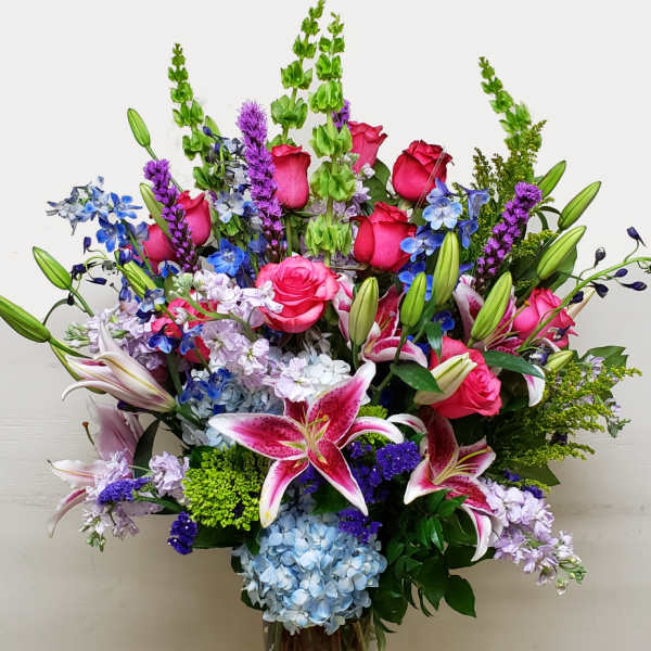 Large mixed bouquet with pink roses, lilies, and blue flowers in a glass vase