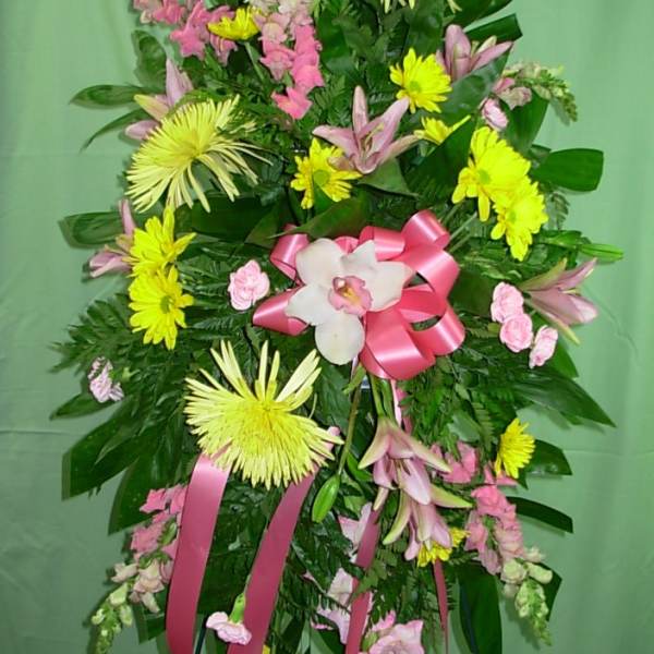 Standing floral spray with pink and yellow flowers and a pink ribbon bow