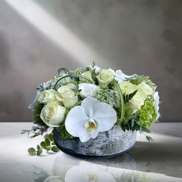 White roses and orchids arranged in a low round vase