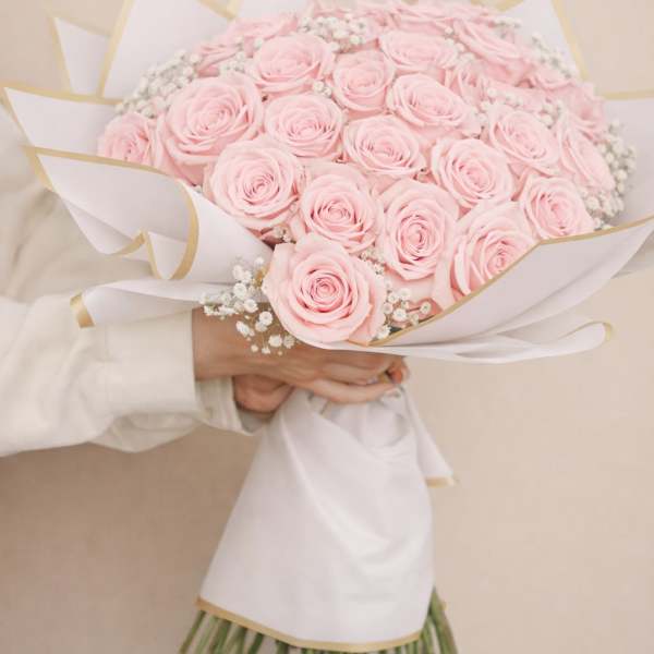 Bouquet of pale pink roses wrapped in white paper with gold trim