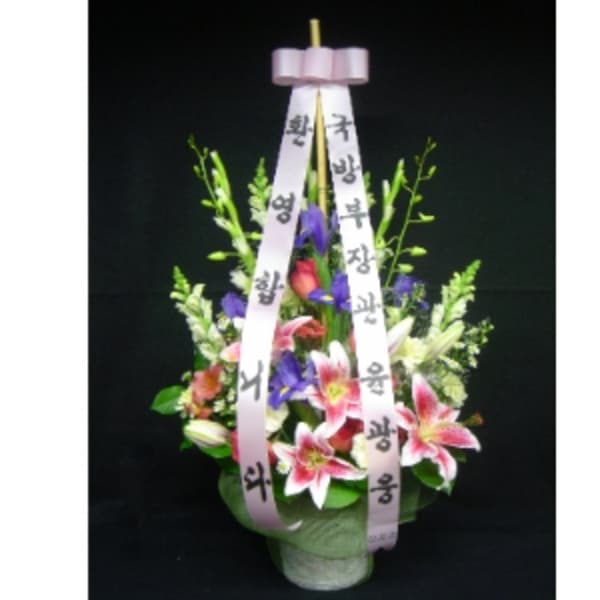 Tall floral arrangement with pink lilies and purple flowers in a pot, accented by long Korean message ribbons.