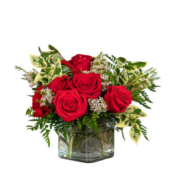 Red roses arranged in a clear glass vase with variegated greenery