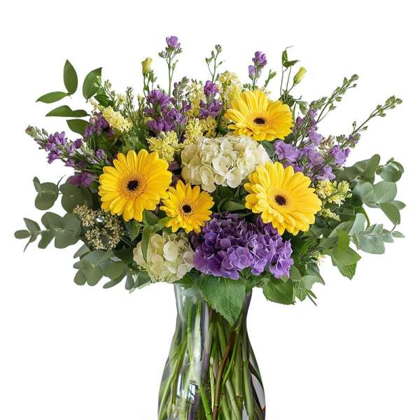 Bouquet of yellow gerbera daisies and purple flowers in a glass vase