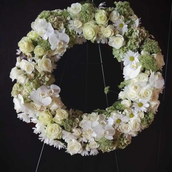White floral wreath on a stand with roses, orchids, and daisies