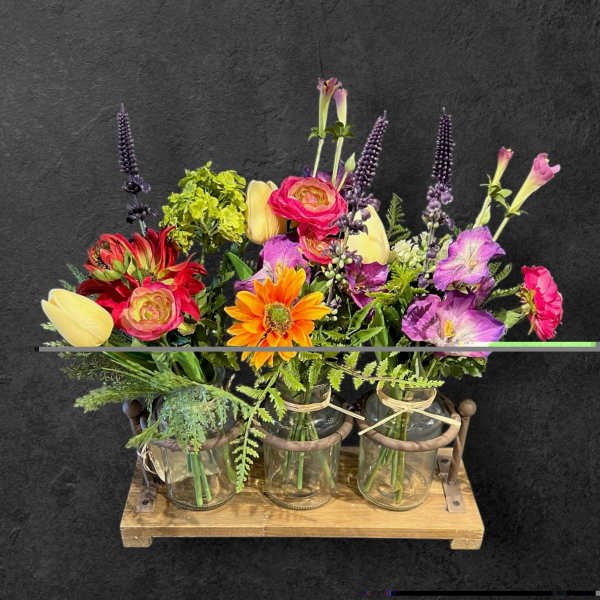 Three small floral arrangements in glass jars on a wooden tray