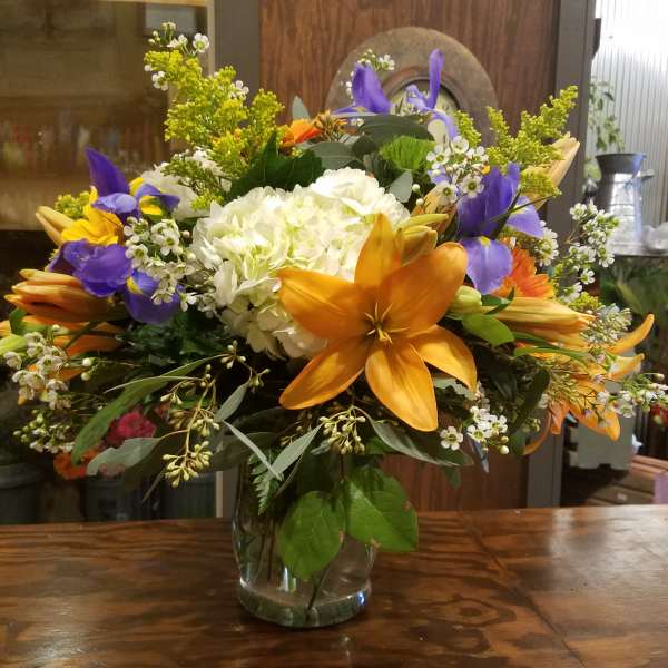 Mixed bouquet in a clear glass vase with orange lilies and purple irises