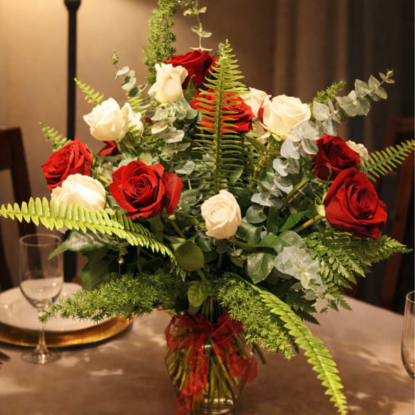 Red and white roses arranged in a glass vase with ferns