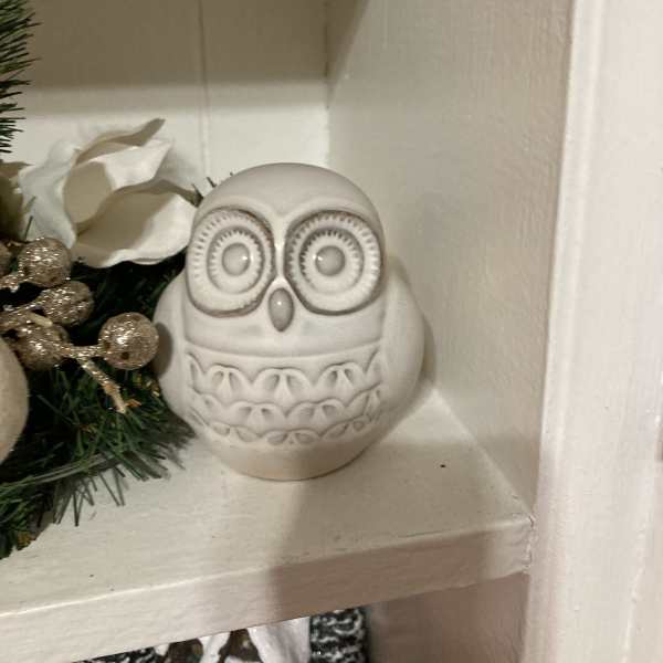 White ceramic owl figurine on a shelf beside holiday greenery